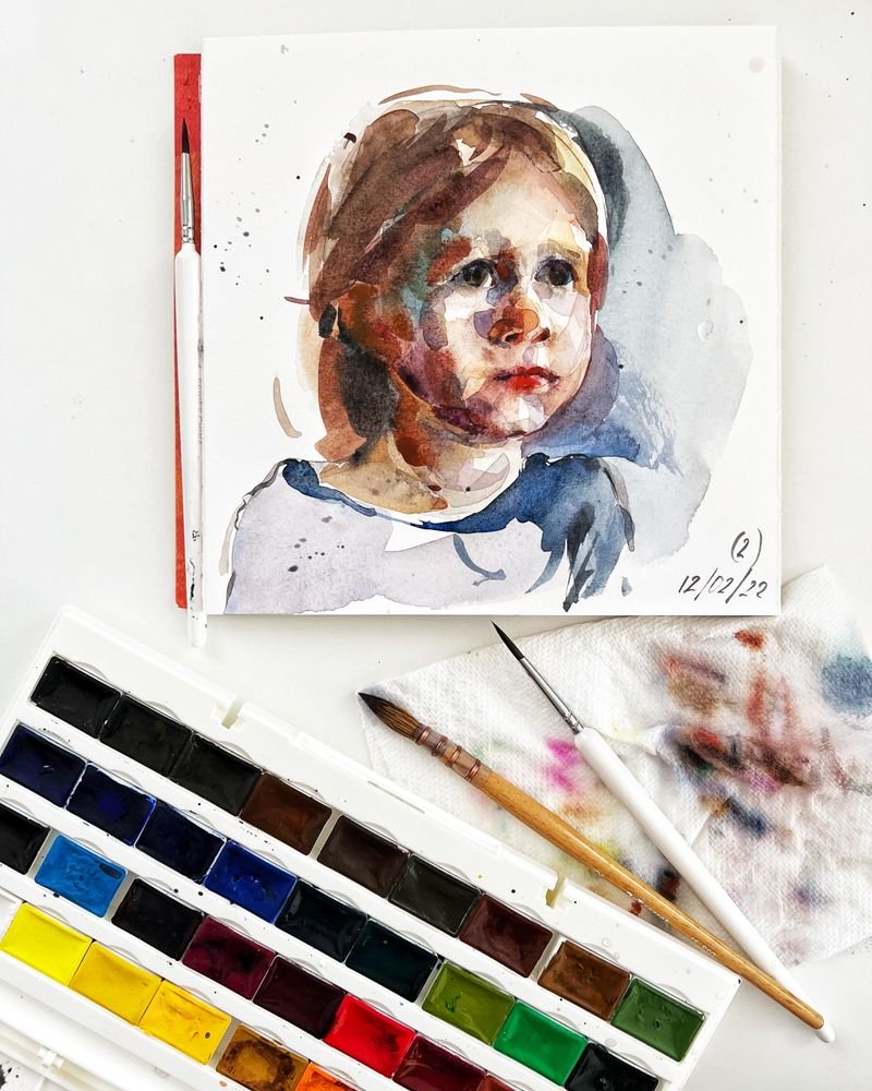 A watercolor portrait of a child beside a paint palette and brushes