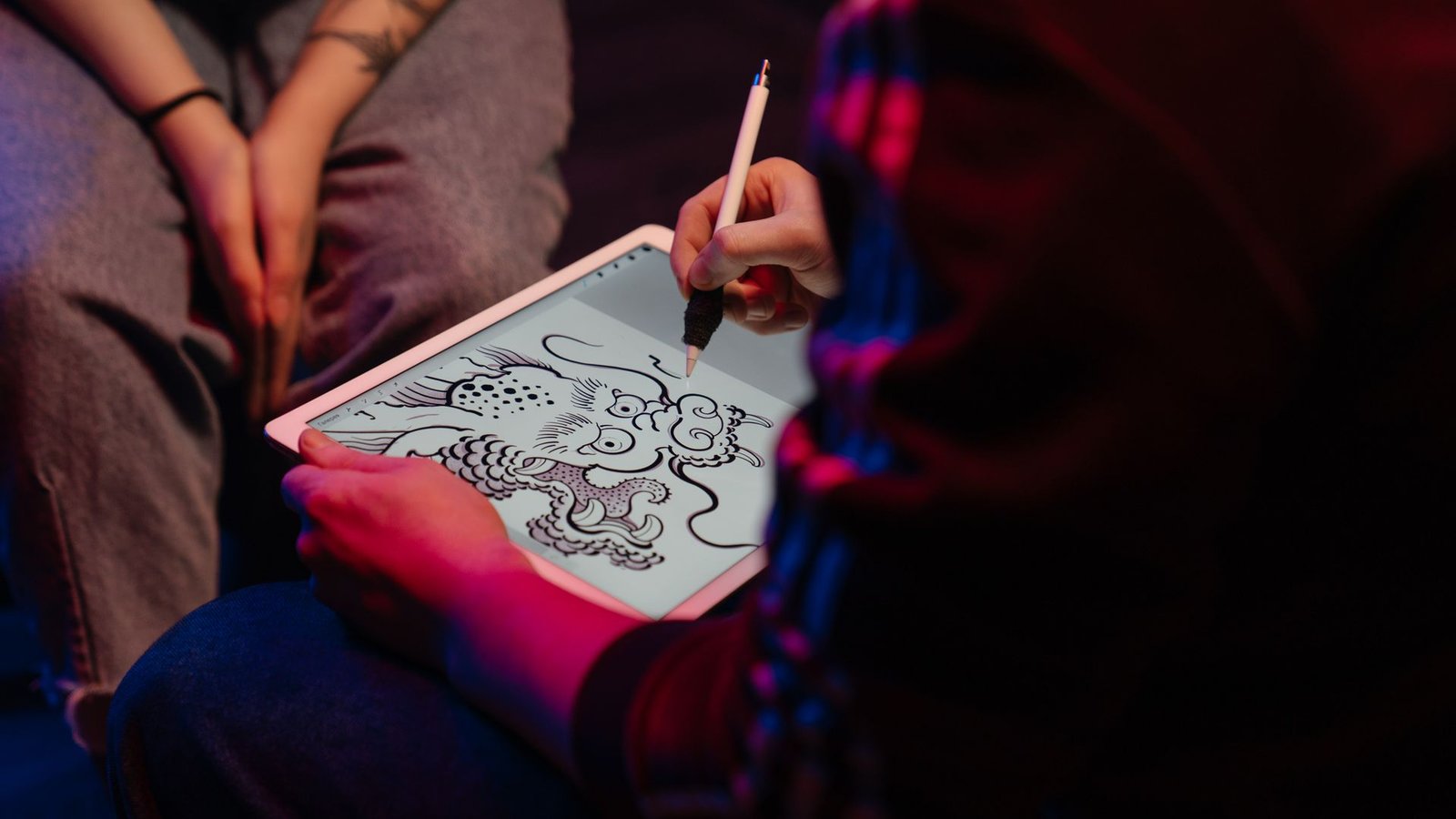 A digital artist drawing an illustration on a tablet under warm neon studio lighting